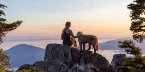 Eine Frau sitzt mit ihrem Hund auf einem Stein