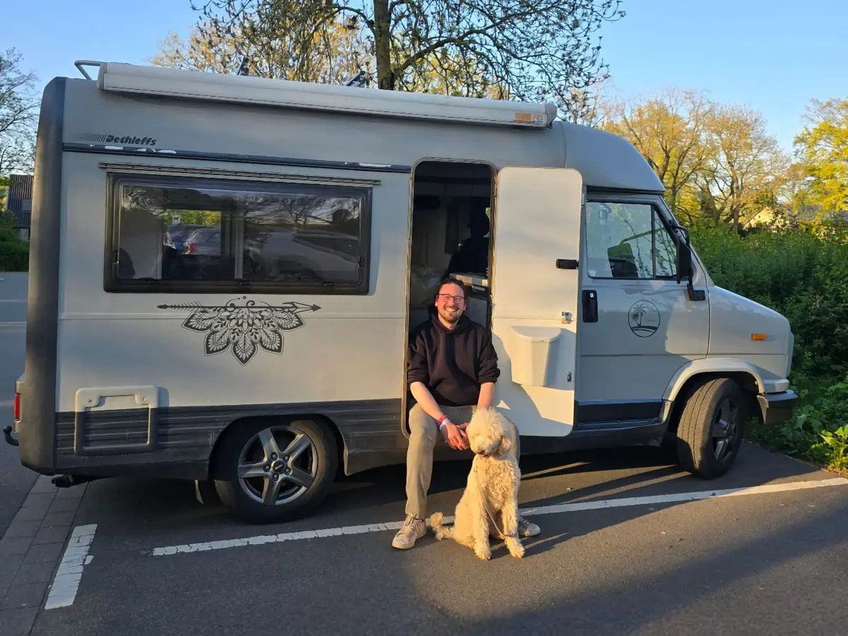 David sitting in the open door of his camper van, with his dog Alva sitting in front of him