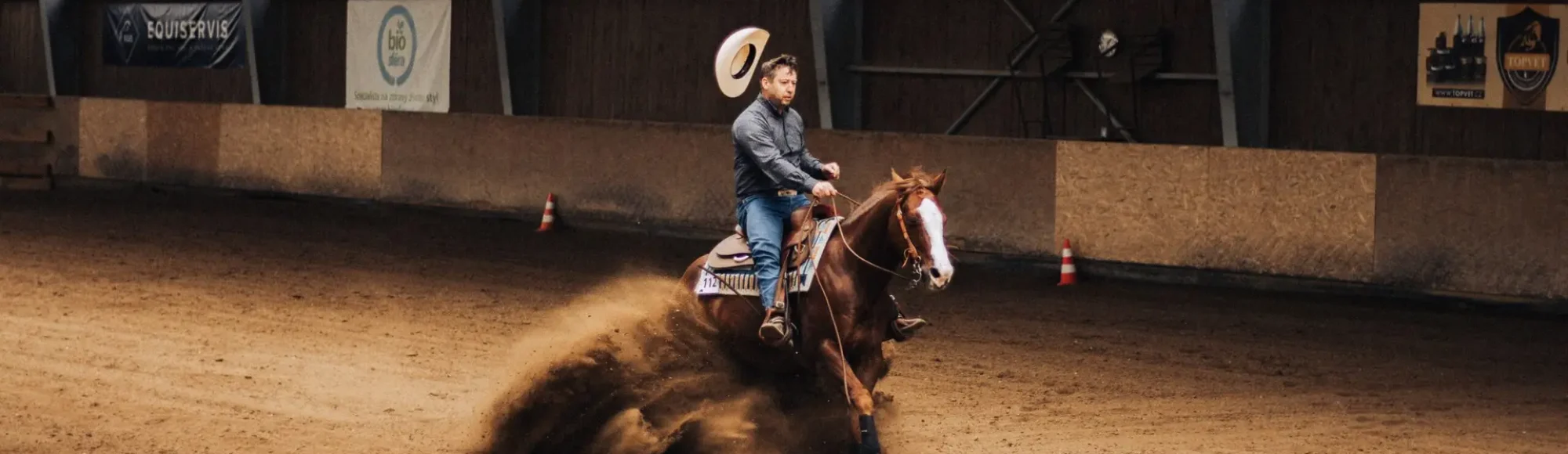 Cowboy performs a sliding stop on a chestnut quarter horse in an indoor arena for reining competition